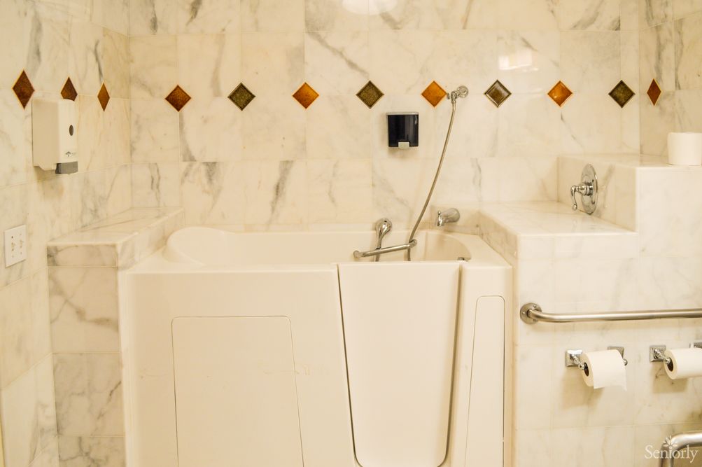 A bathroom featuring an accessible walk-in bathtub with a marble wall and safety grab bar.