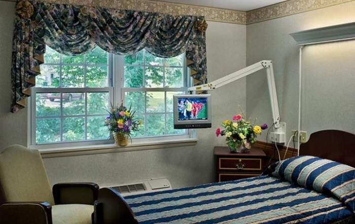 A well-decorated hospital room with a bed, television, and floral arrangements near the window.