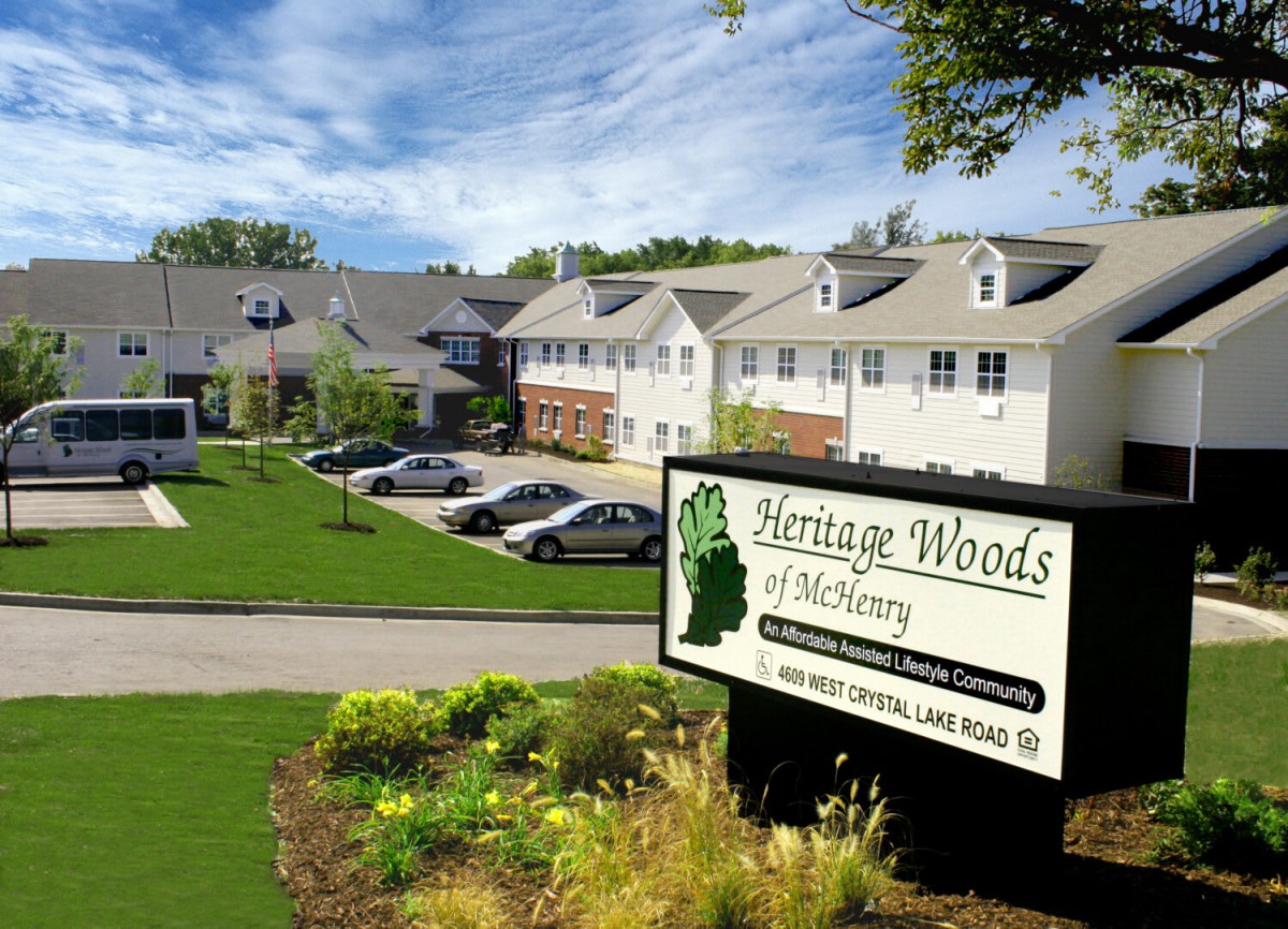 A view of residential buildings with a parking area and a sign reading 'Heritage Woods'.