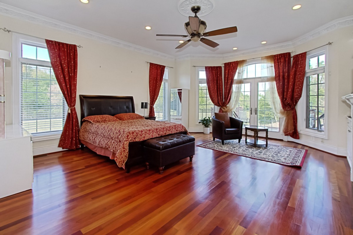 Spacious bedroom with wooden floors, large windows, and elegant red curtains.