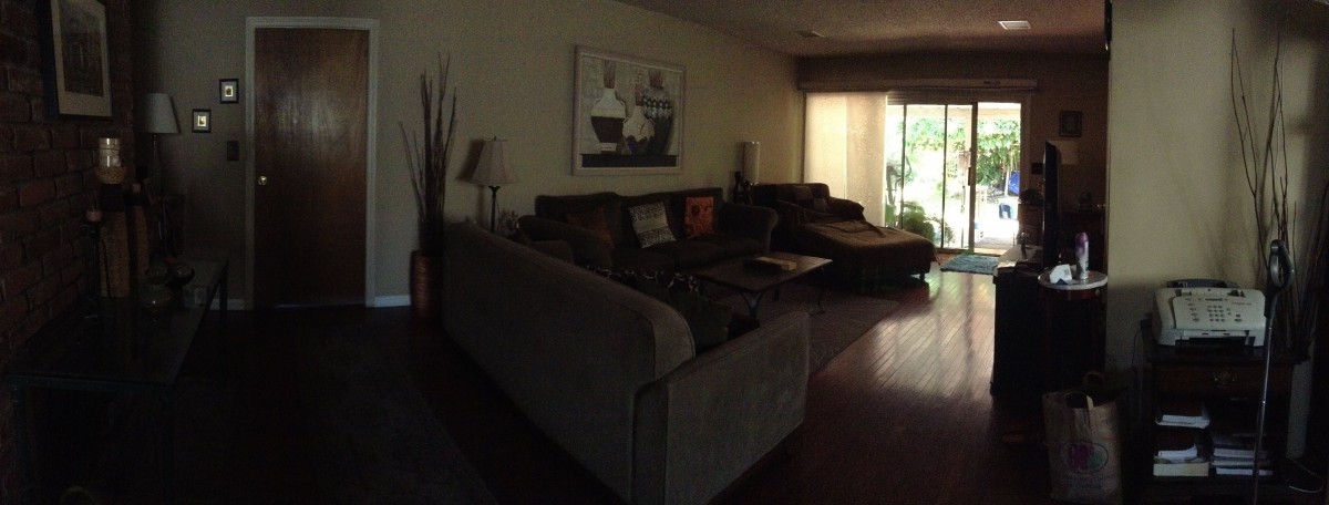 A dimly lit living room with a large sofa, wall artwork, and natural light coming from a window.