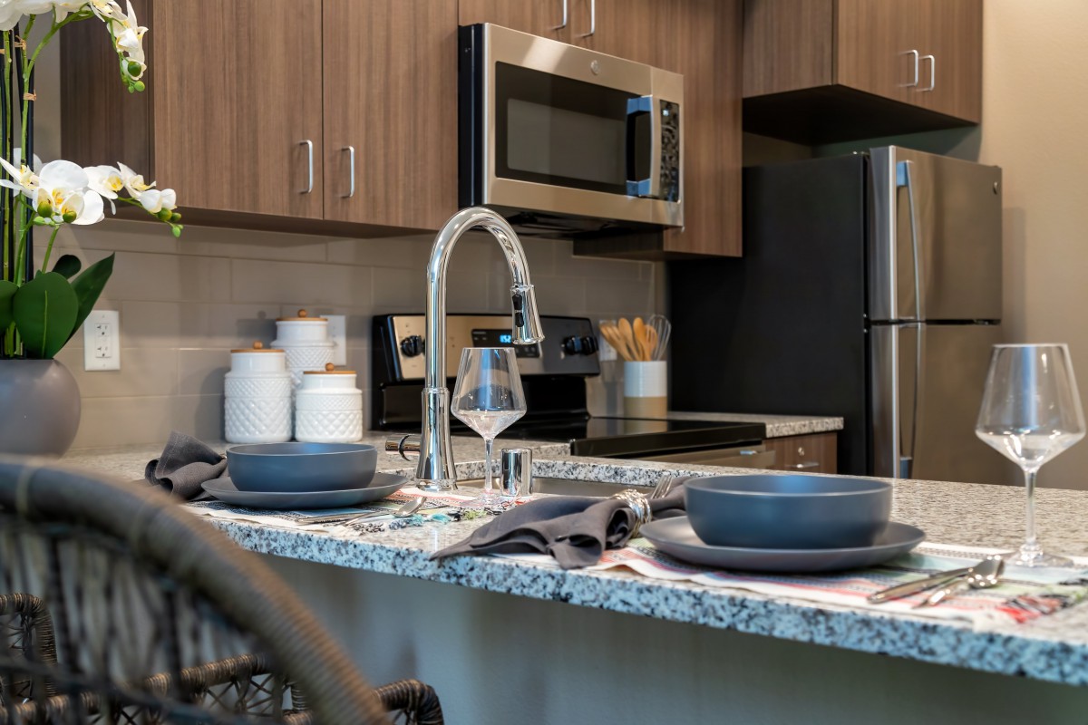 A modern kitchen with wooden cabinets, a granite countertop, and stainless steel appliances.