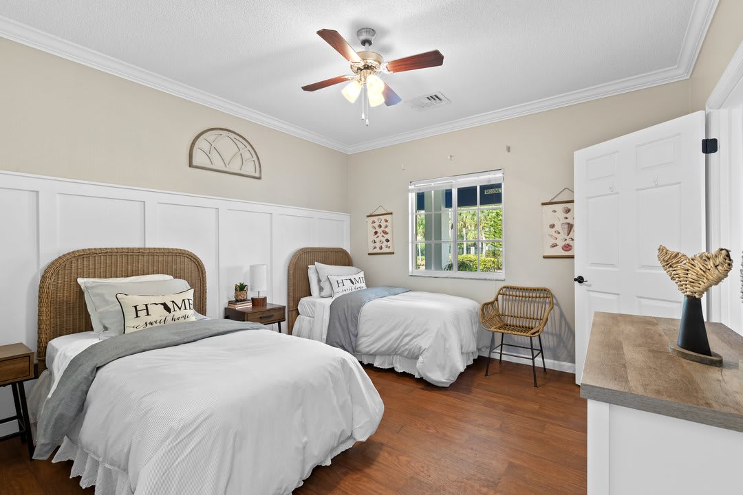 A cozy bedroom with twin beds, decorative pillows, and a ceiling fan.