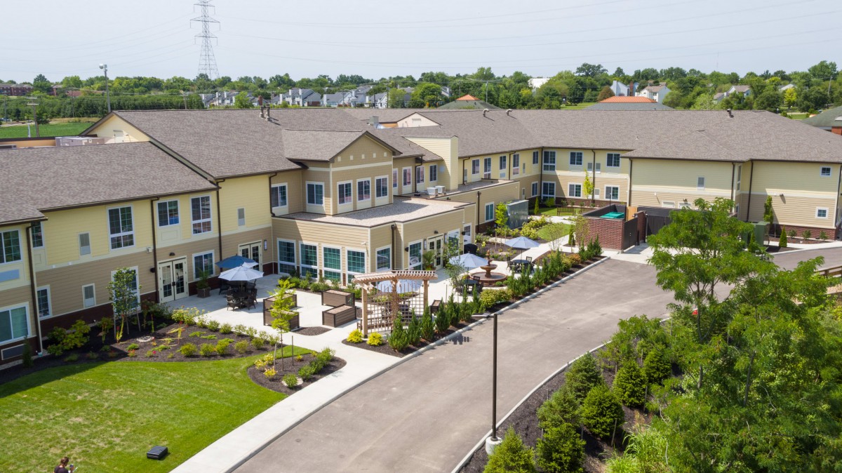 Aerial view of a residential building surrounded by landscaped greenery and a driveway.