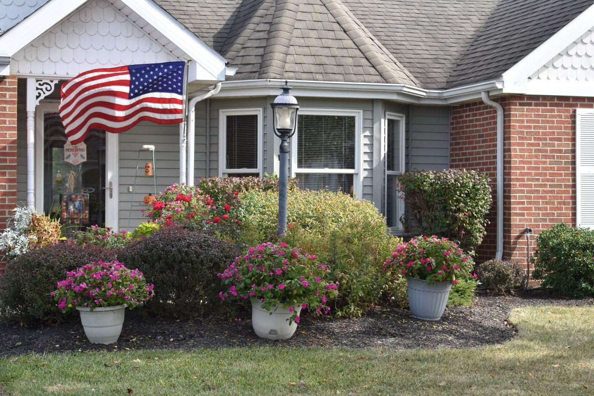 A suburban house with a well-maintained garden, featuring an American flag and various potted plants and shrubs.
