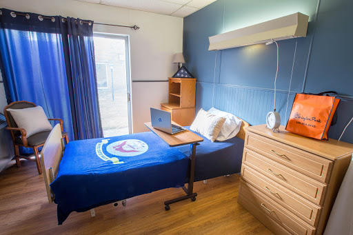 A cozy bedroom featuring a neatly made bed, a laptop on a small desk, and warm wooden furniture.
