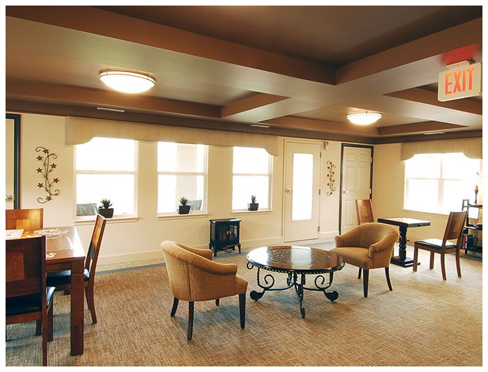 A cozy living room featuring armchairs, a round glass table, and ample natural light through multiple windows.