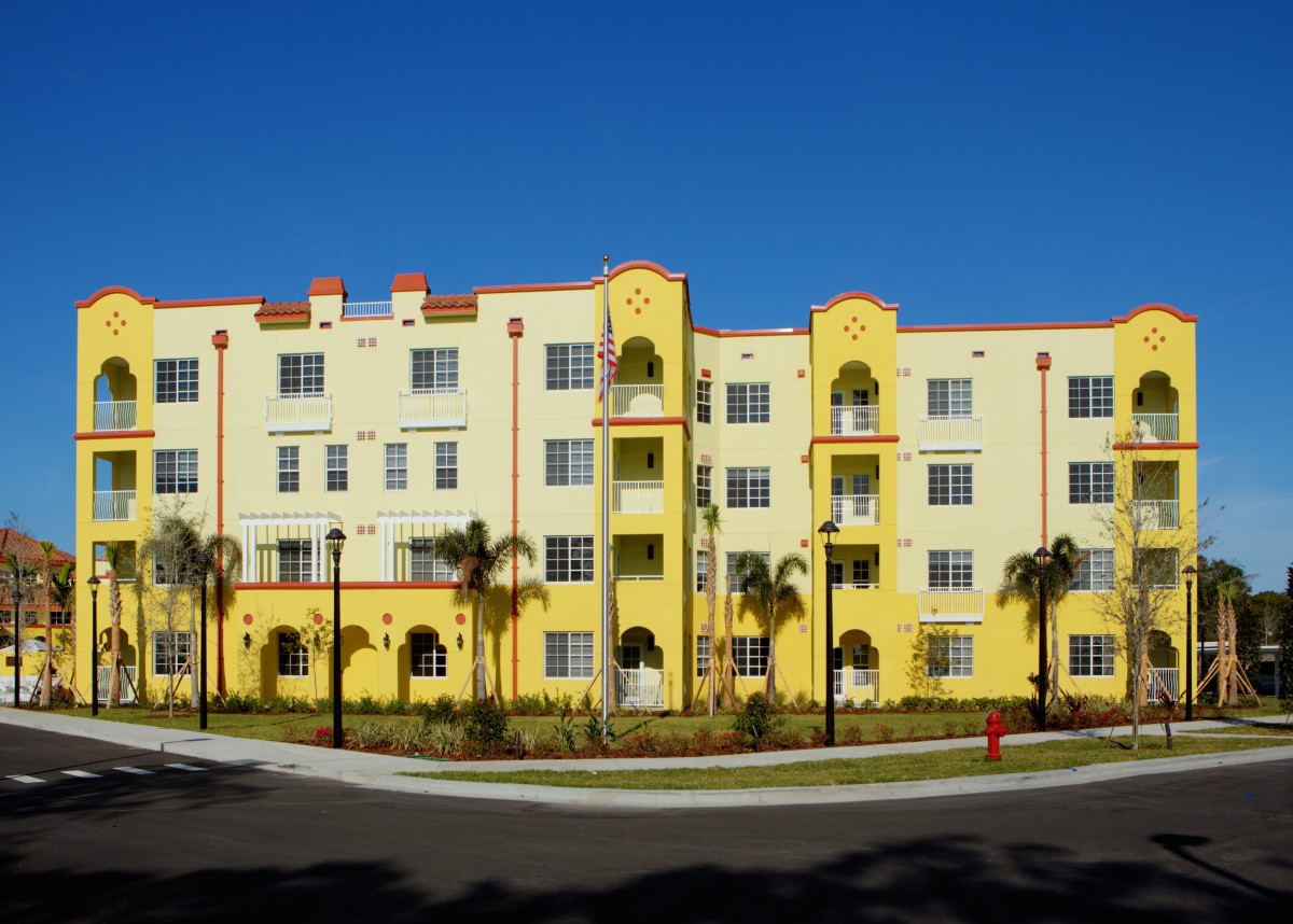 A brightly colored yellow apartment building surrounded by palm trees under a clear blue sky.