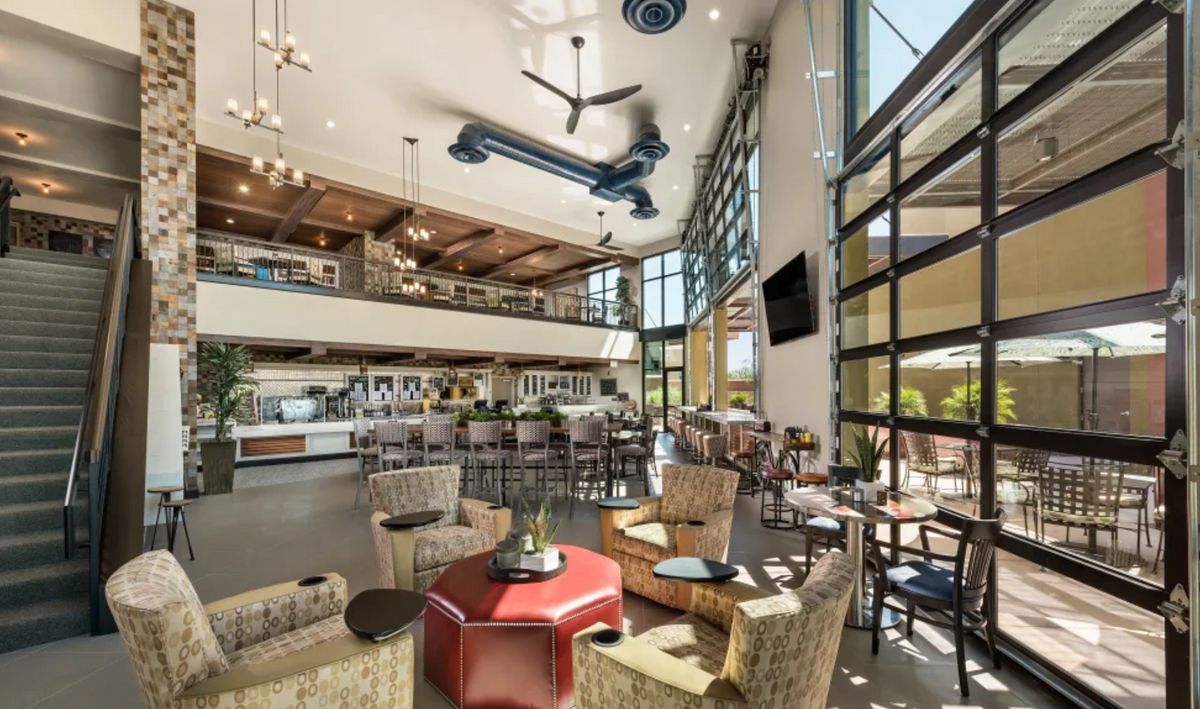 A modern restaurant interior with high ceilings and ample natural light, featuring a dining area and bar.