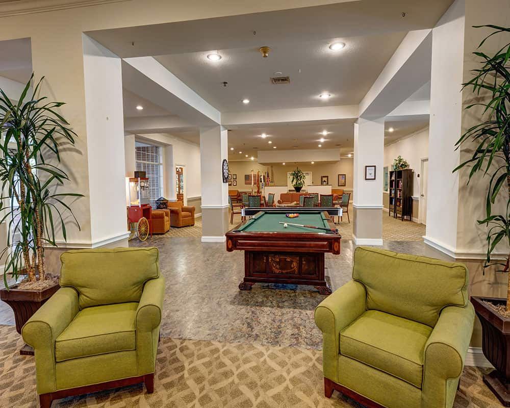 A cozy lounge area featuring a pool table surrounded by comfortable seating and warm lighting.