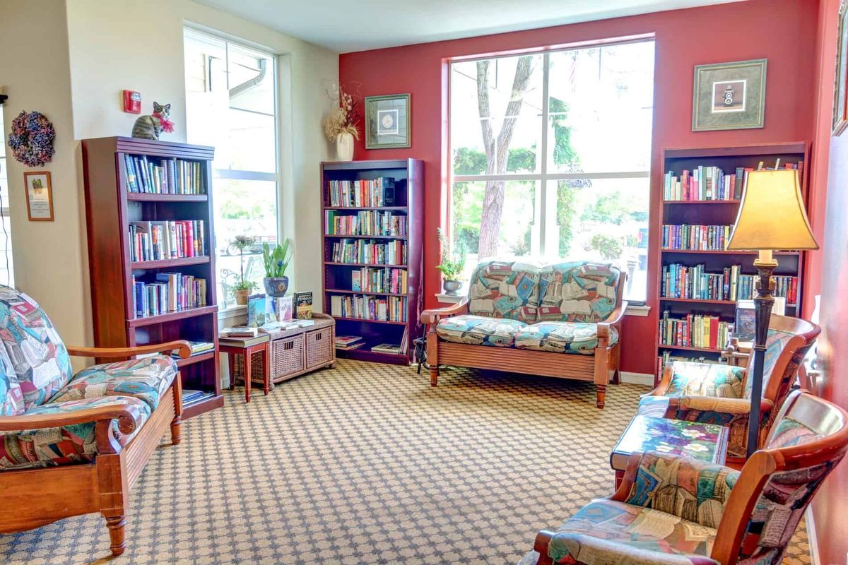 A cozy library reading area with bookshelves, sofas, and large windows.