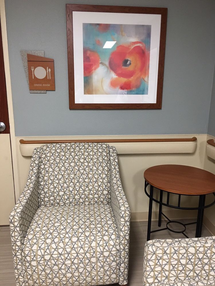 A waiting room with patterned chairs, a small table, and colorful artwork on the wall.