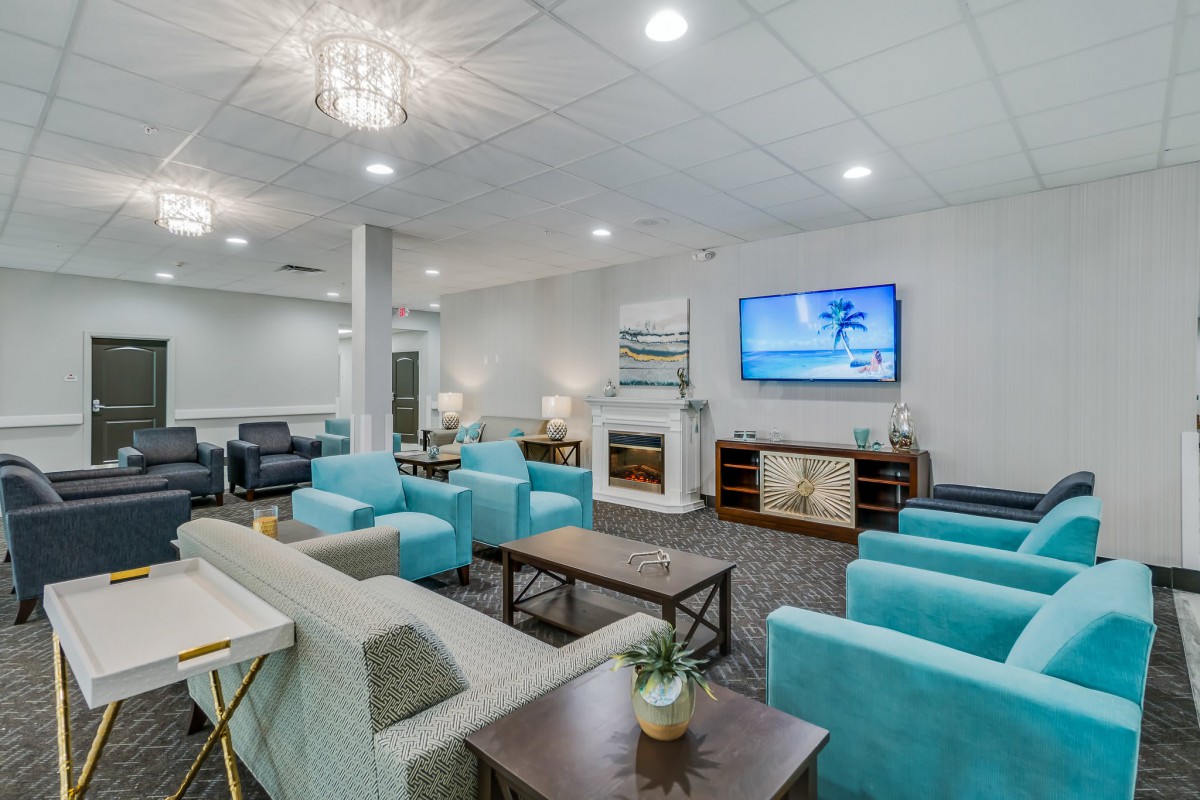 A modern lounge with turquoise chairs and sofas, featuring a TV and stylish decor.