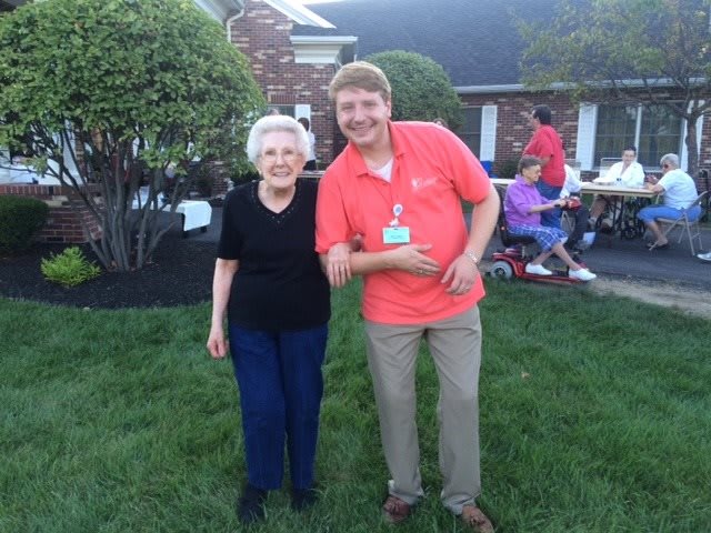 Two people smiling and posing together outdoors near a house.