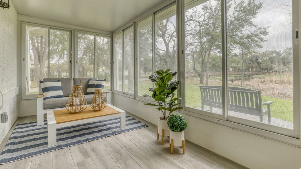 A cozy sunroom with large windows, featuring potted plants and a stylish wooden floor.