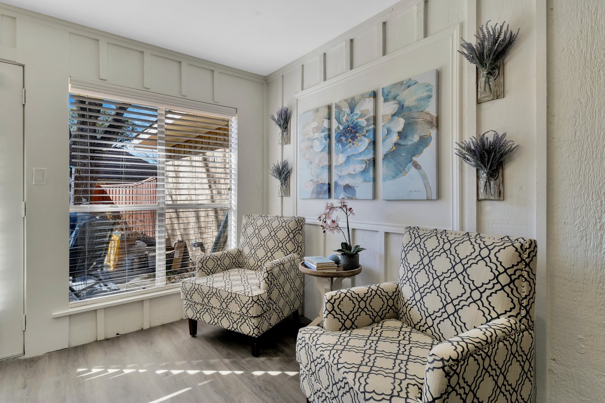 A cozy living room with patterned chairs, wall art, and ample natural light.