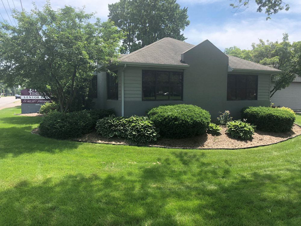 A well-maintained house with a lush green lawn and neatly trimmed bushes on a sunny day.