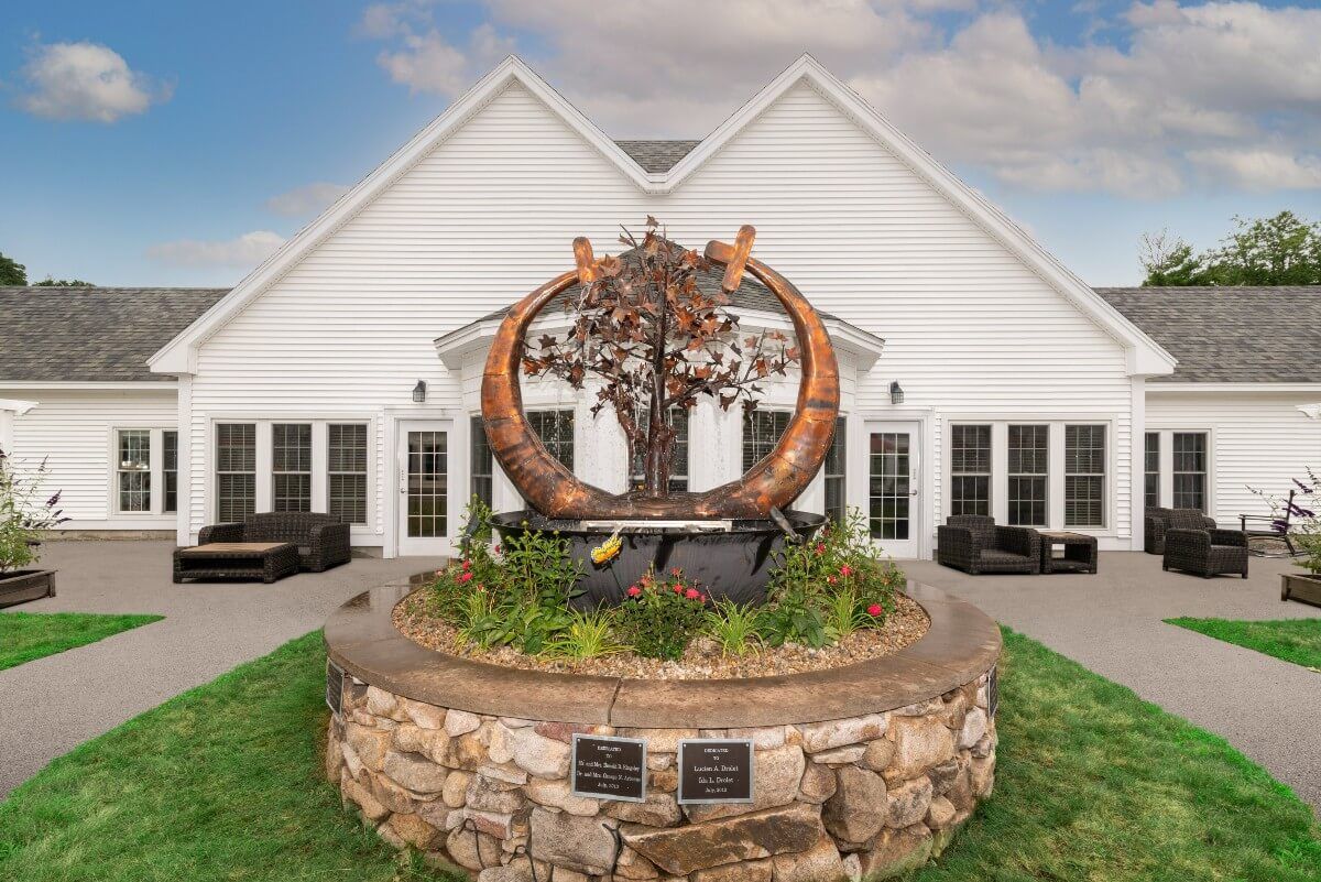 An intricate sculpture displayed in front of a white building, surrounded by a landscaped garden.
