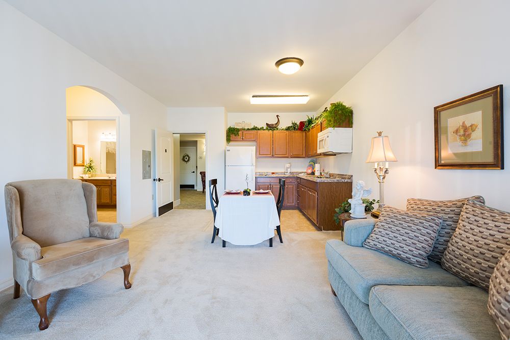 A cozy apartment with an open living room and kitchen area, featuring comfortable seating and bright lighting.
