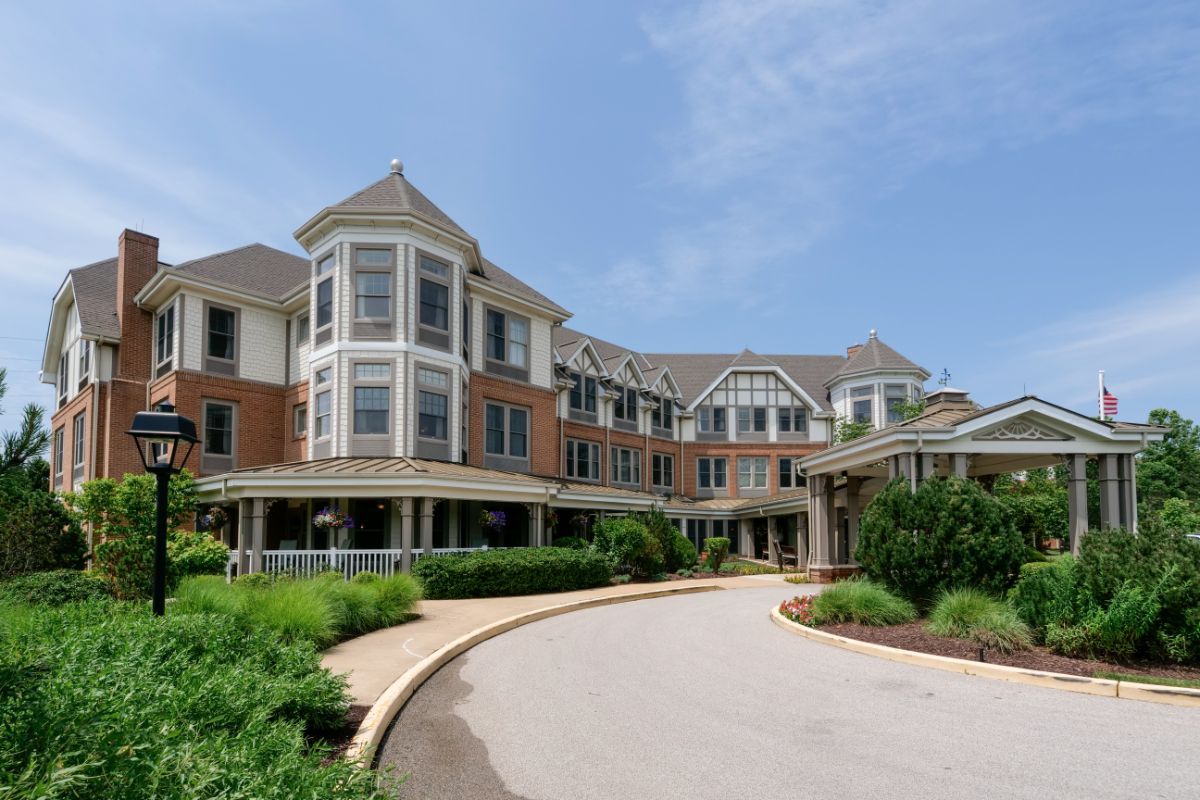 A large residential building with a circular driveway and landscaped gardens under a clear blue sky.