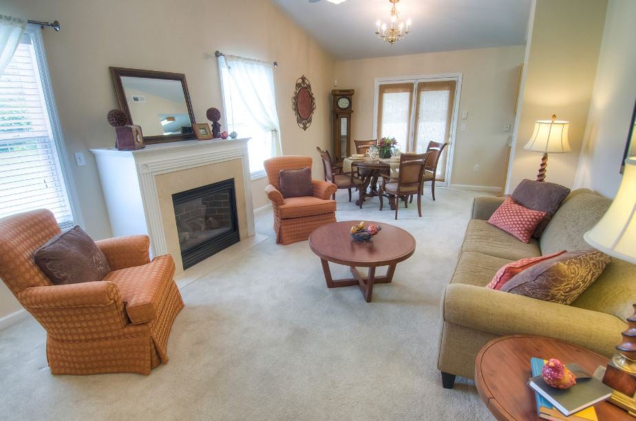 A cozy living room with a fireplace, sofa, chairs, and a dining area.