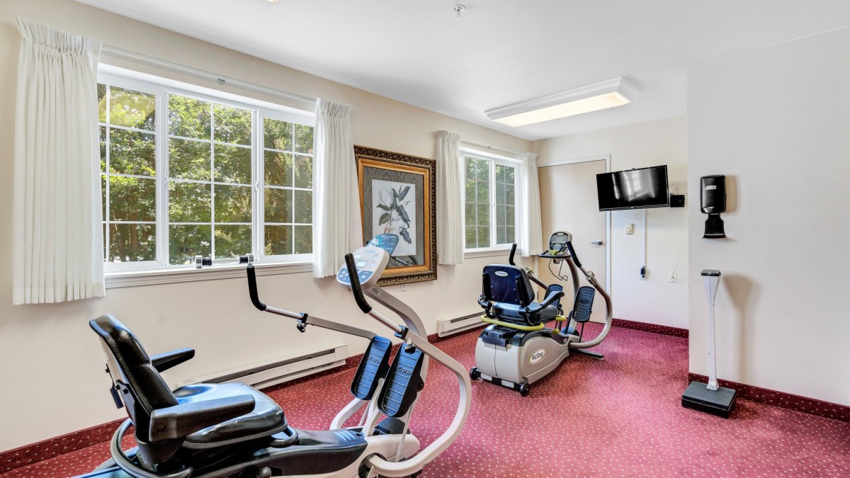 A bright gym room with exercise equipment including an elliptical machine and a stationary bike.