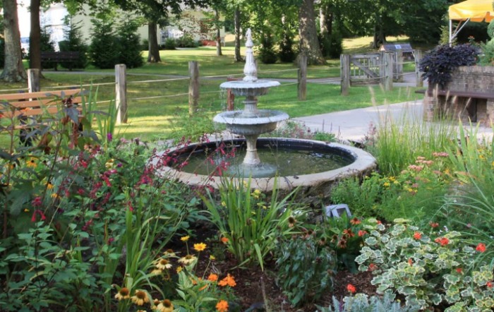 A beautiful garden scene featuring a two-tiered fountain surrounded by vibrant flowers and lush greenery.