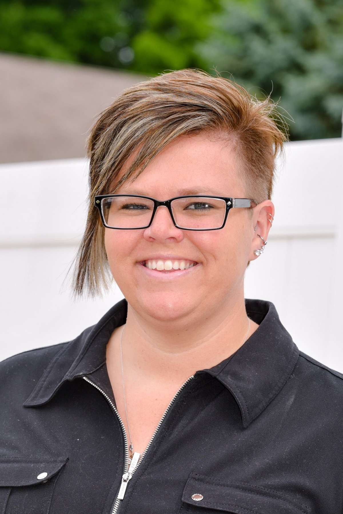 A person with short hair and glasses smiling outdoors.