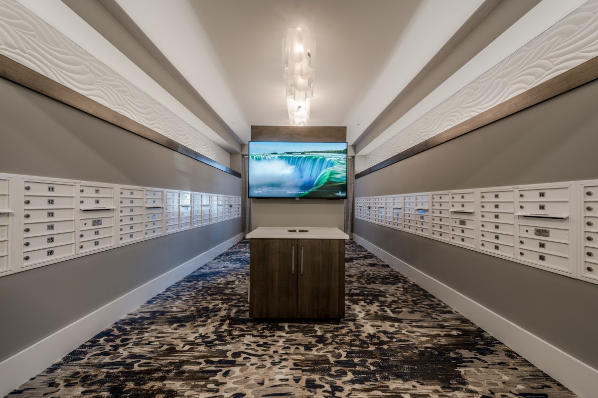 A modern hallway with mailboxes lining the walls and a central screen display.