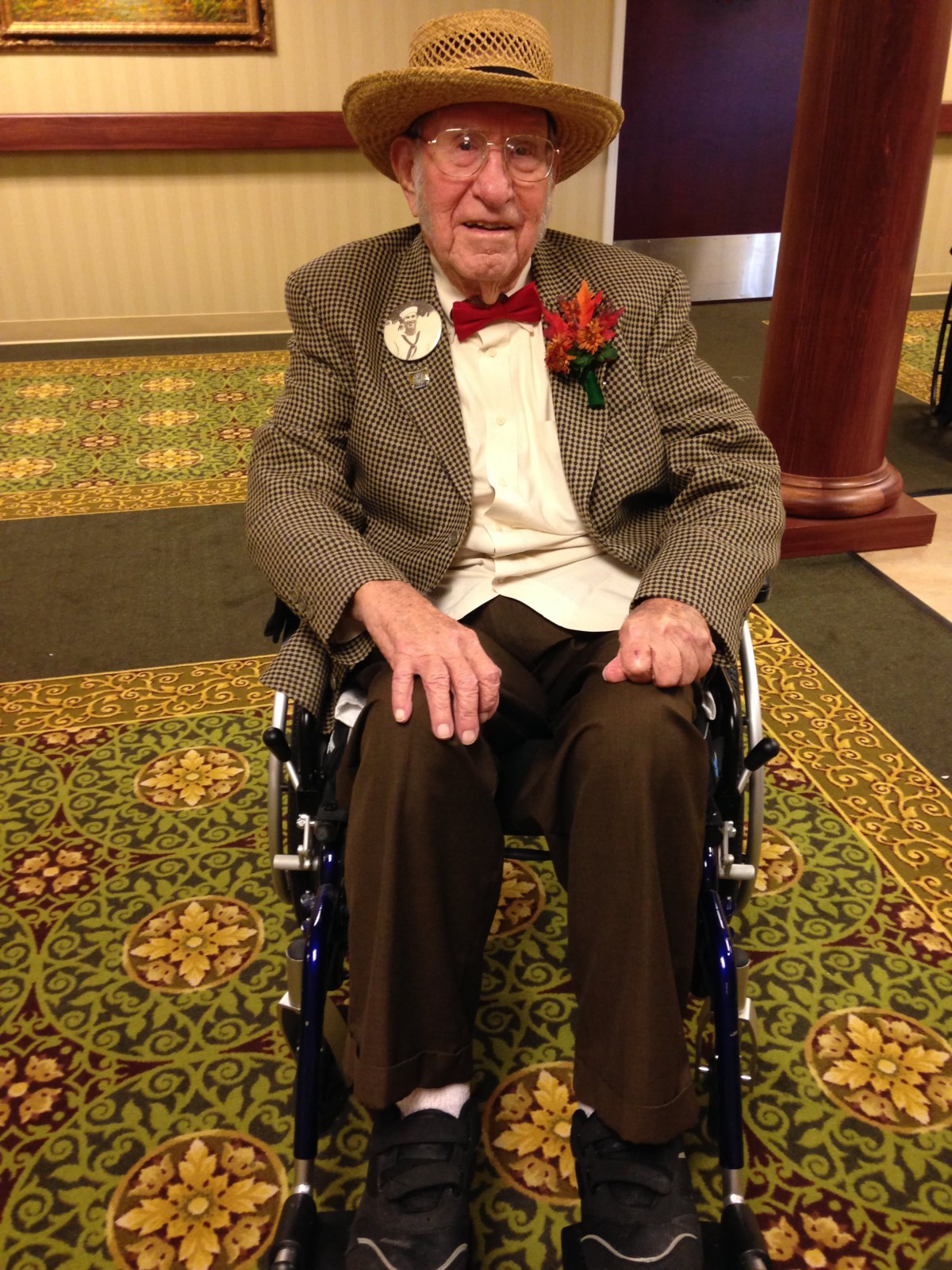 An elderly person dressed in formal attire sitting in a wheelchair indoors.