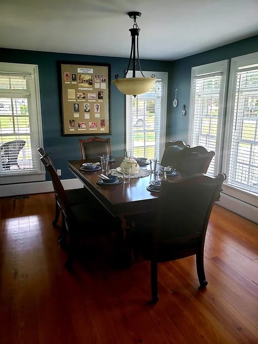 A well-lit dining room with a wooden table, chairs, and large windows.