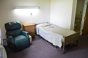 A simple hospital room featuring a bed, chair, and minimal medical equipment.