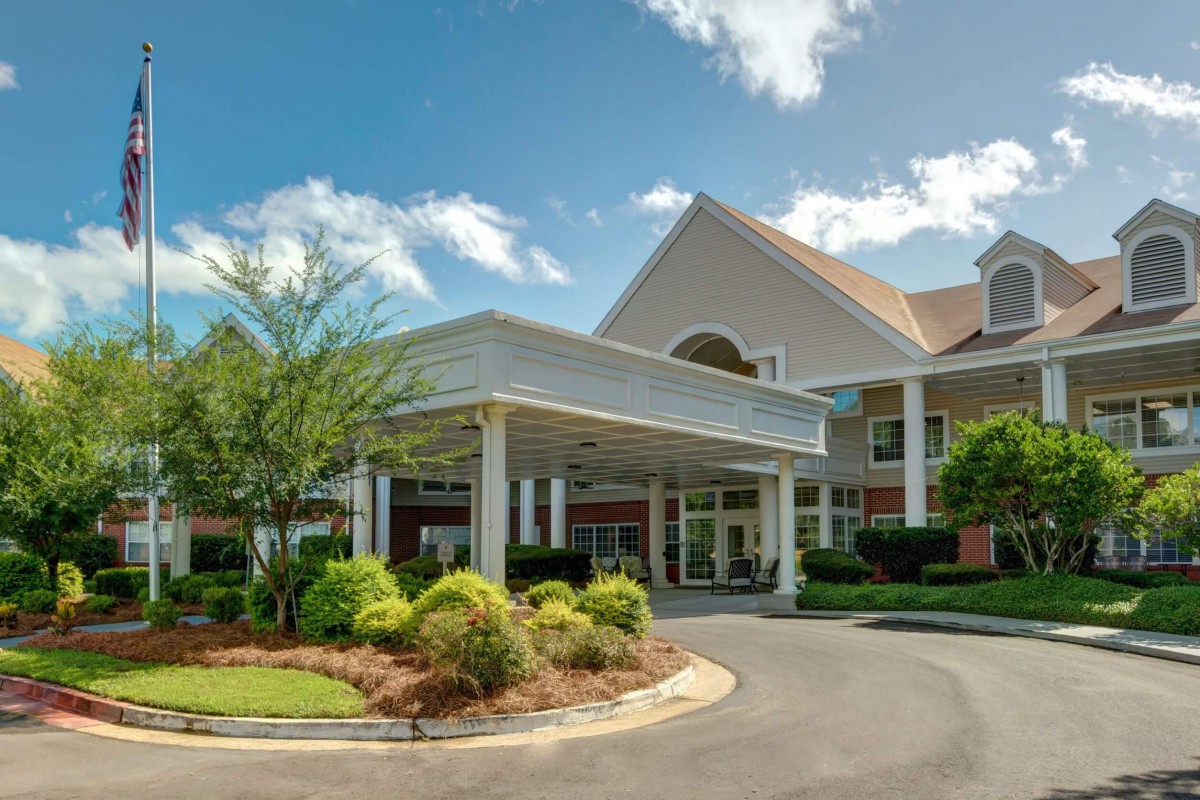 A well-maintained building entrance with landscaped surroundings under a partly cloudy sky.