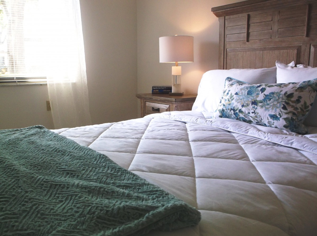 A cozy bedroom with a neatly made bed and a soft lamp on the bedside table.