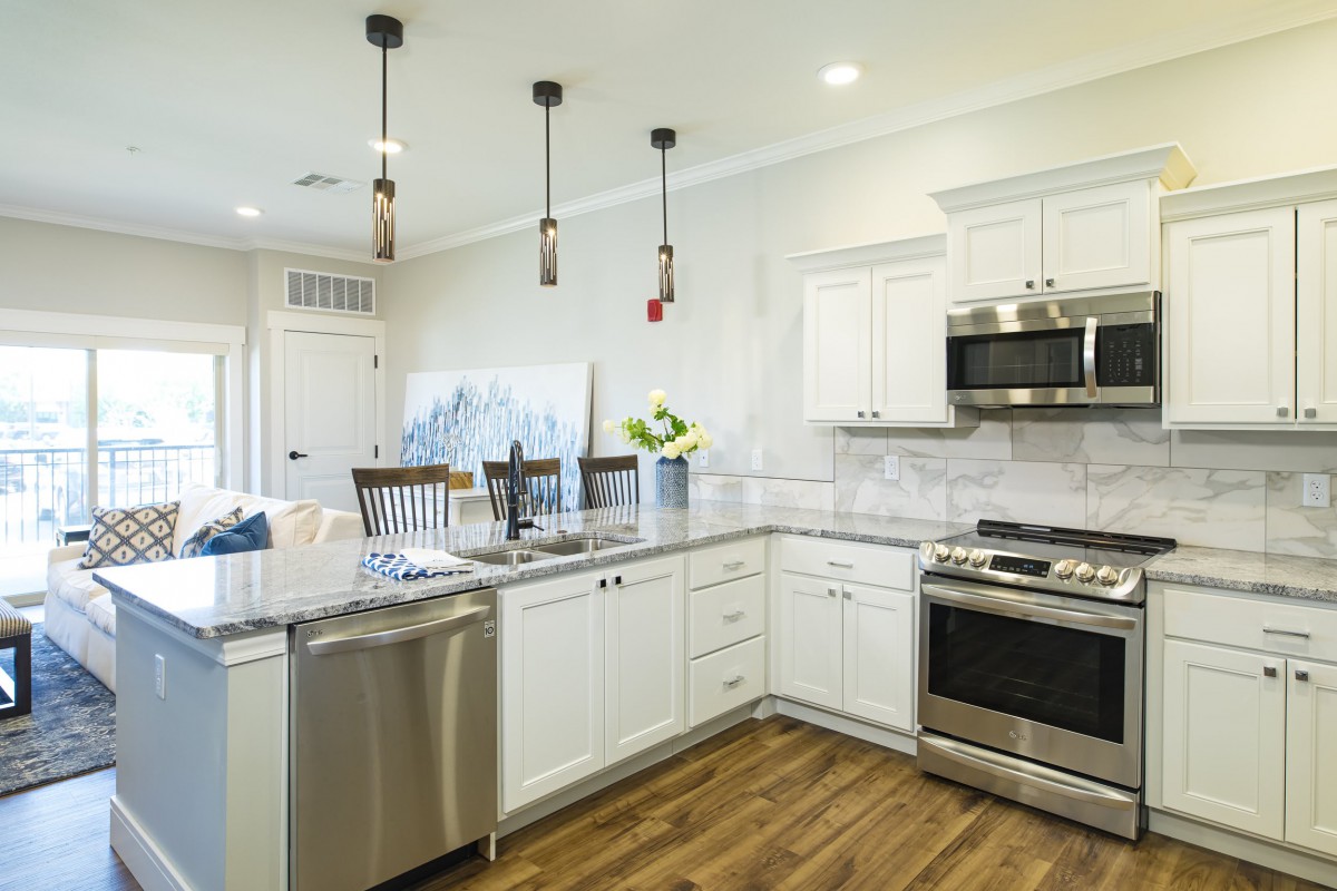 A modern kitchen with white cabinets, stainless steel appliances, and wood flooring.
