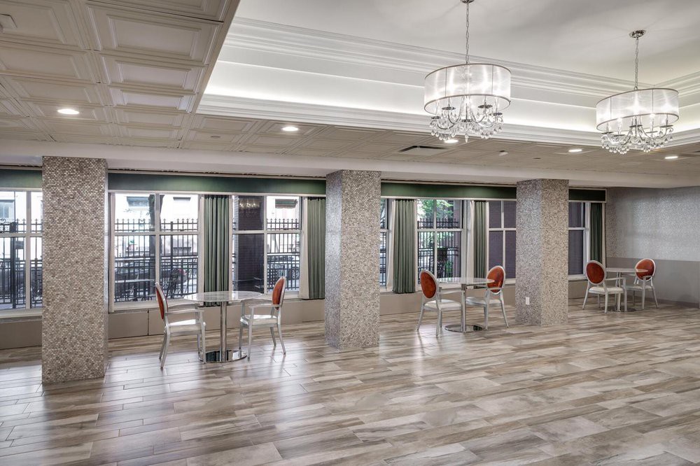A spacious, modern lobby area with a chandelier, tables, and chairs near large windows.