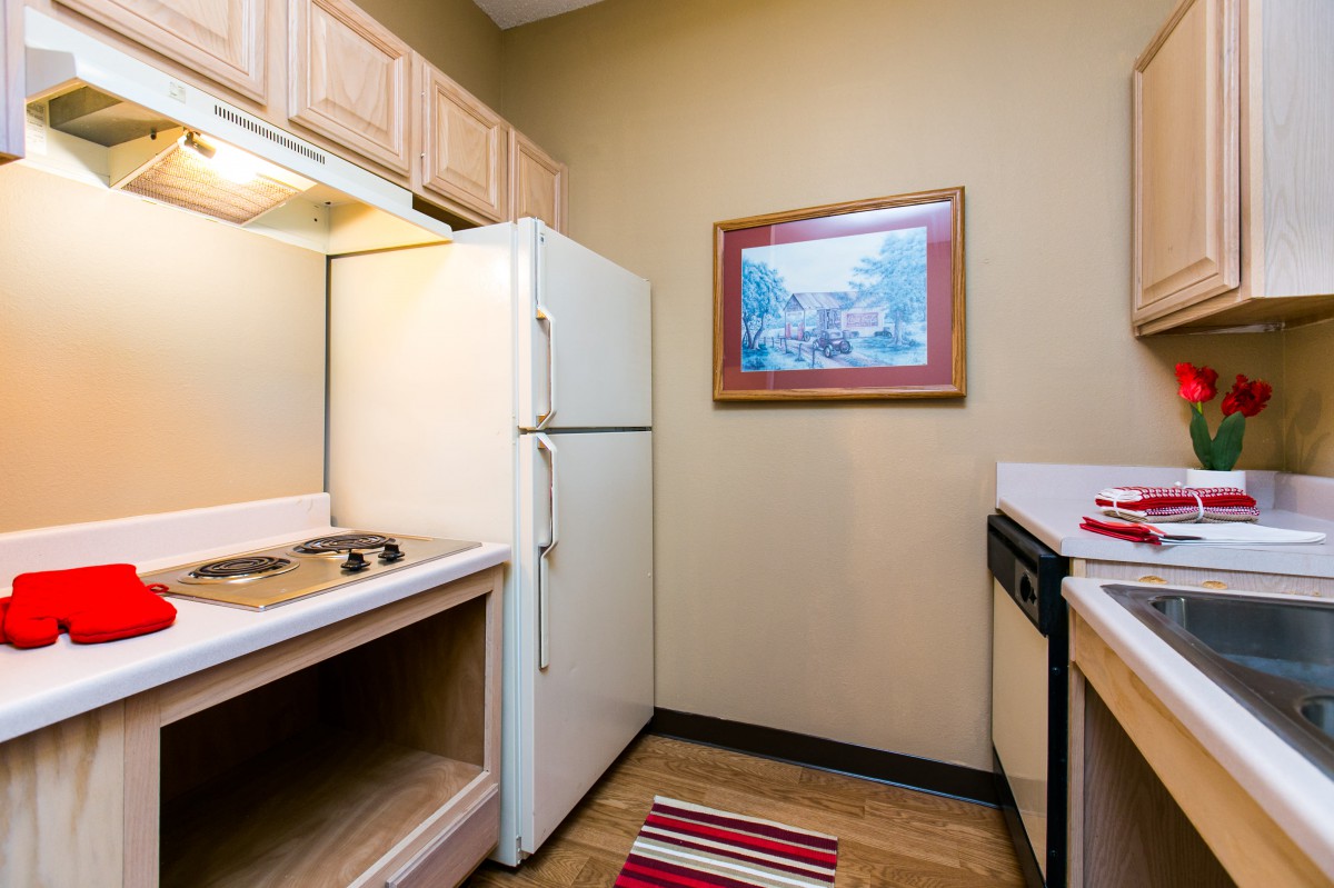 A compact kitchen featuring a refrigerator, sink, and countertop with wooden cabinets.