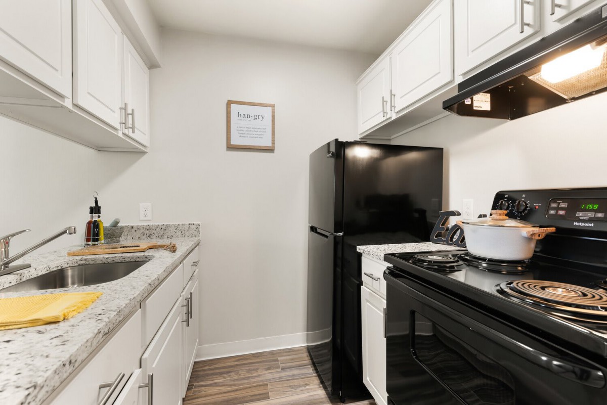 A modern, compact kitchen with white cabinets and black appliances.