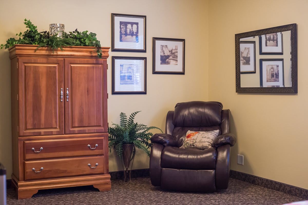 A cozy living room corner featuring a leather armchair, wooden cabinet, and decorative wall art.