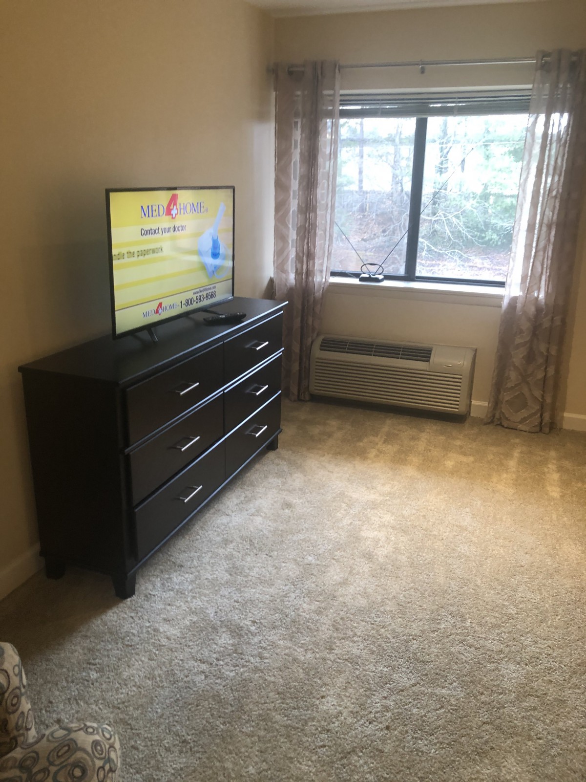 A neatly arranged bedroom with a dresser and television beside a window.