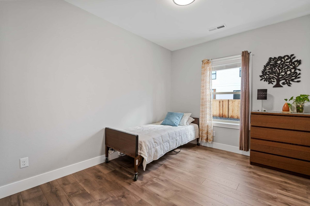A minimalist bedroom featuring a single bed with wooden flooring and a window dressed with curtains.
