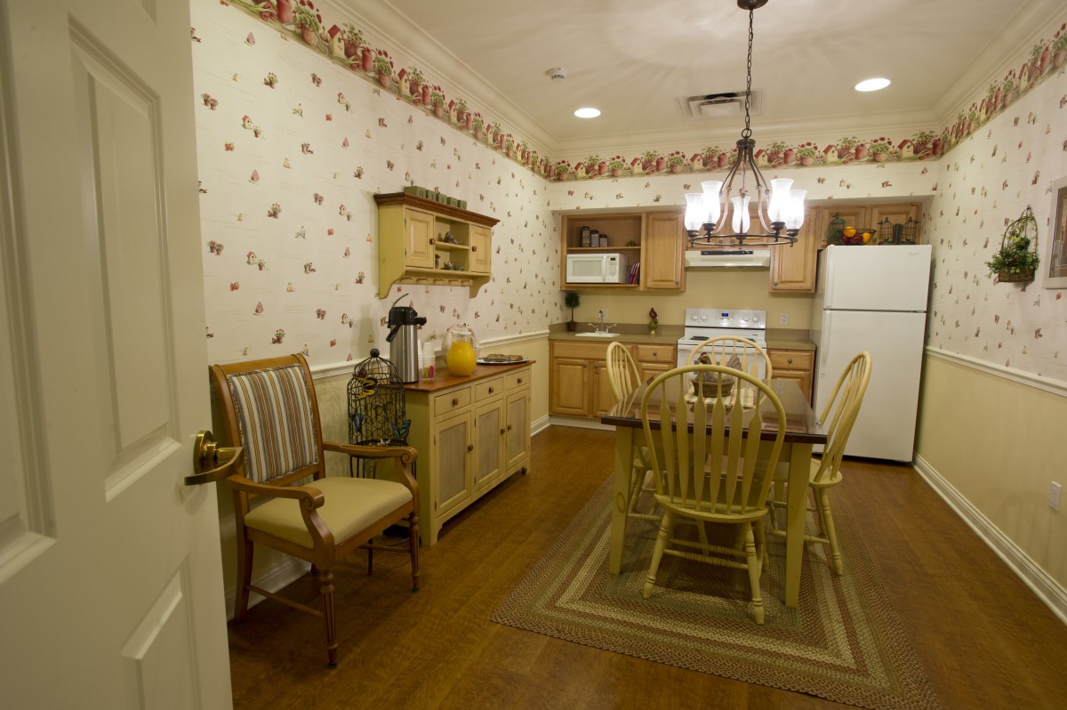 A cozy kitchen and dining area with vintage decor, featuring a wooden dining set, wallpapered walls, and a chandelier.