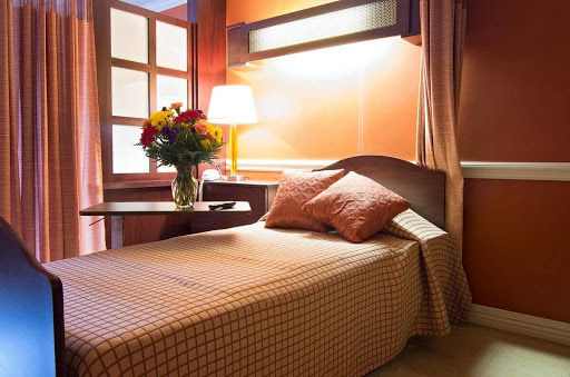 A cozy hotel room featuring a single bed, a bedside table with a lamp, and a fresh bouquet of flowers.