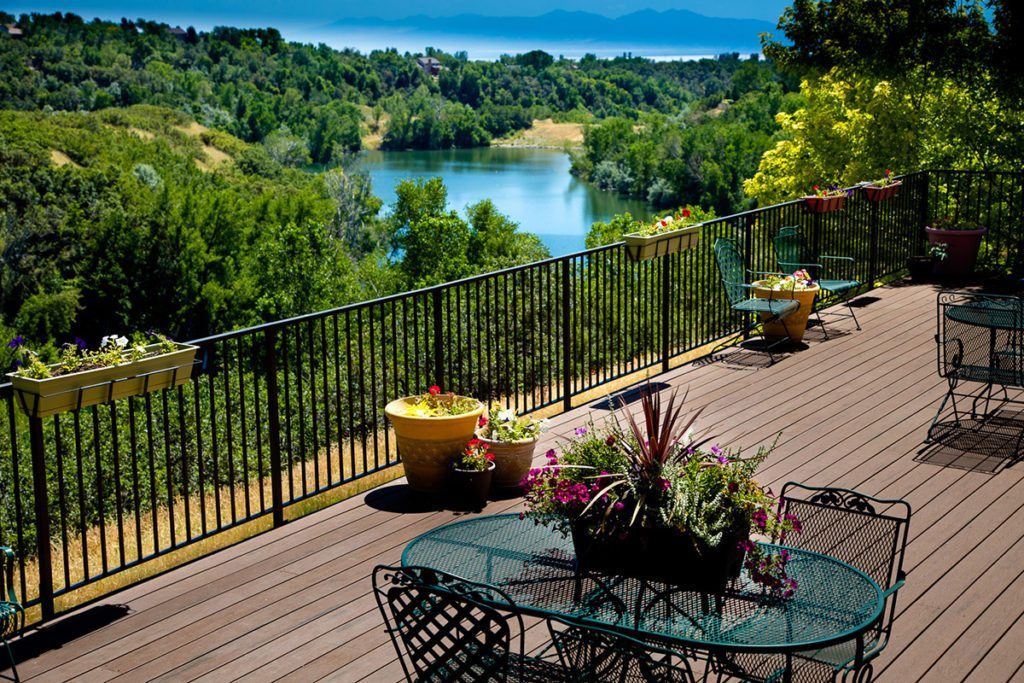A scenic terrace with outdoor seating overlooks a tranquil lake surrounded by lush greenery.
