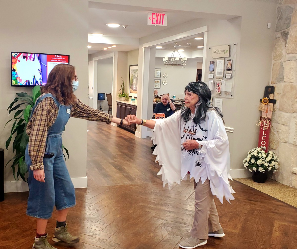 Two people in costumes greet each other with a handshake in a hallway.