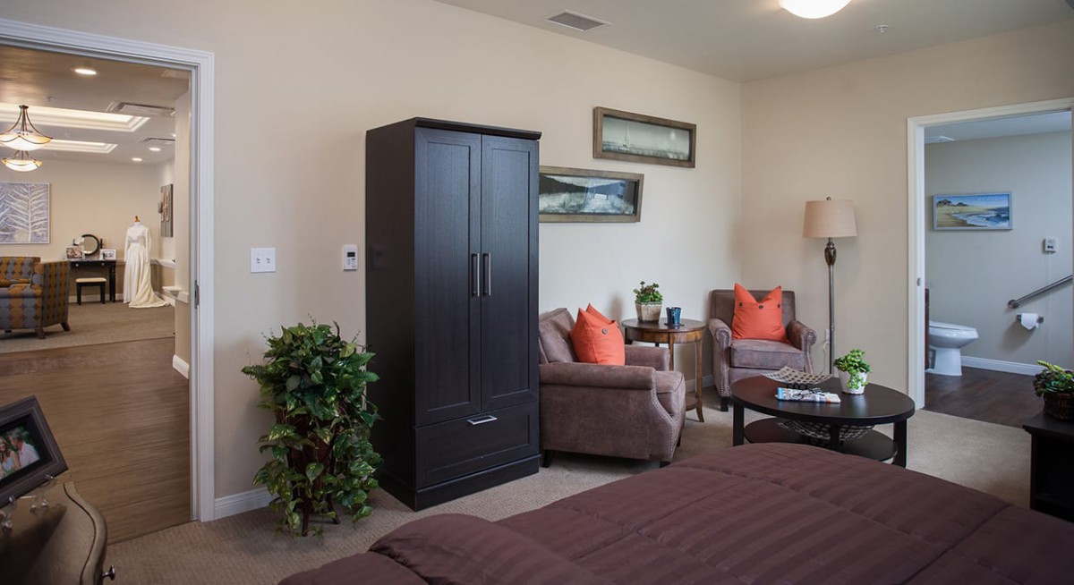 A cozy bedroom with modern furniture, including a wardrobe, two armchairs, and decorative elements such as plants and pictures.