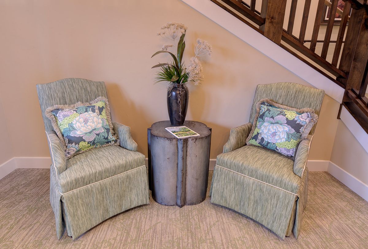 A cozy seating area with two patterned chairs and a small round table topped with a vase of flowers.