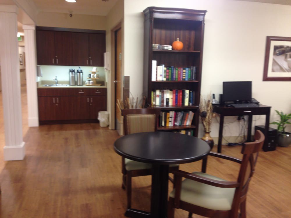 A cozy office space with a round table, bookshelf, and kitchenette in the background.