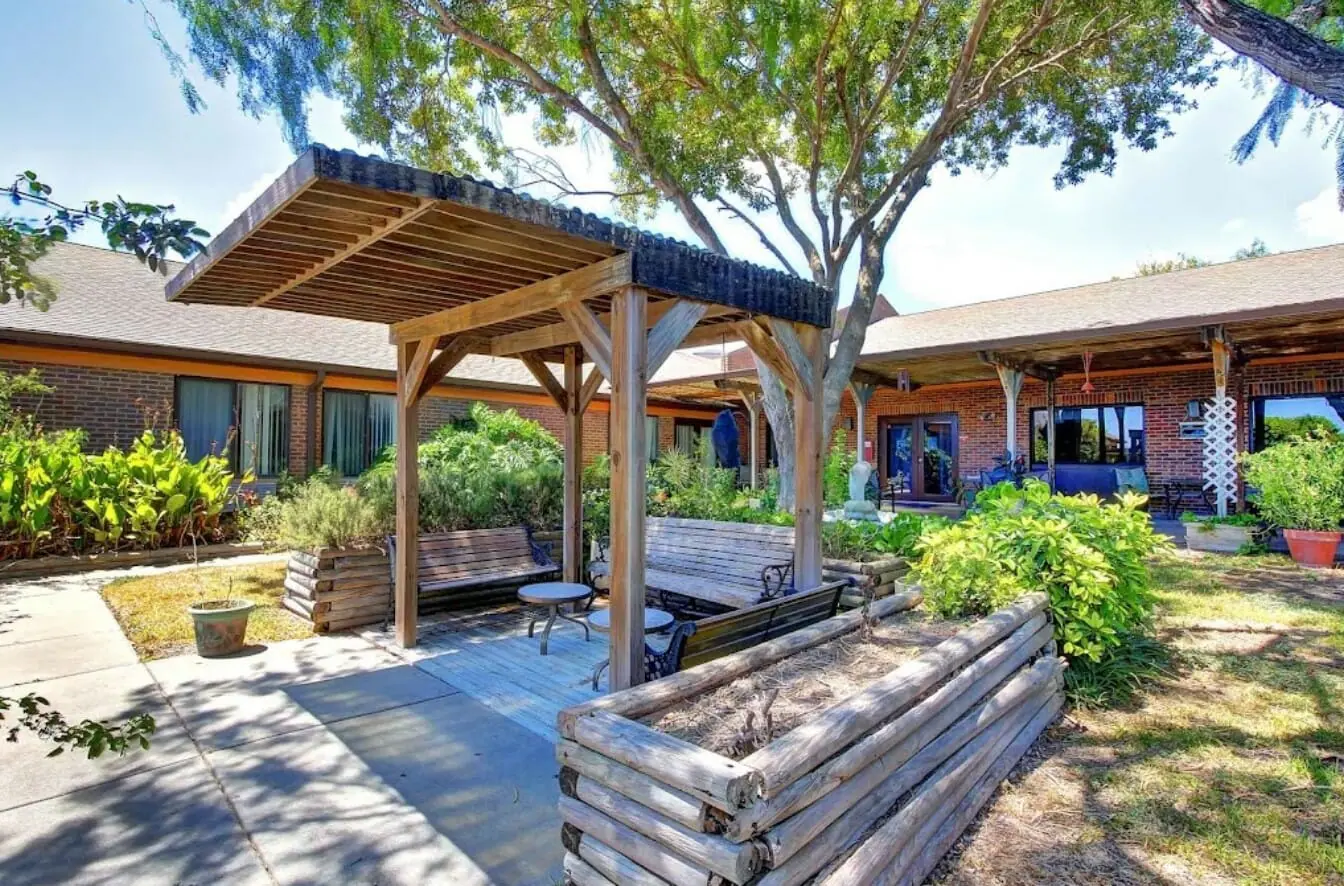 A peaceful garden area featuring a wooden pergola, benches, and lush greenery.