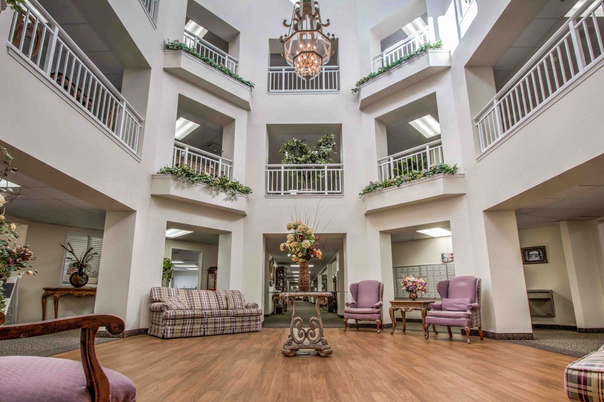 A spacious atrium with elegant lounge furniture, balconies, and a central chandelier.